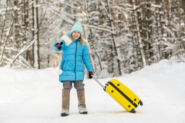 A girl in winter in felt boots goes with a suitcase on a frosty snowy day.