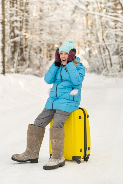 A girl in winter in felt boots sits on a suitcase on a frosty snowy day