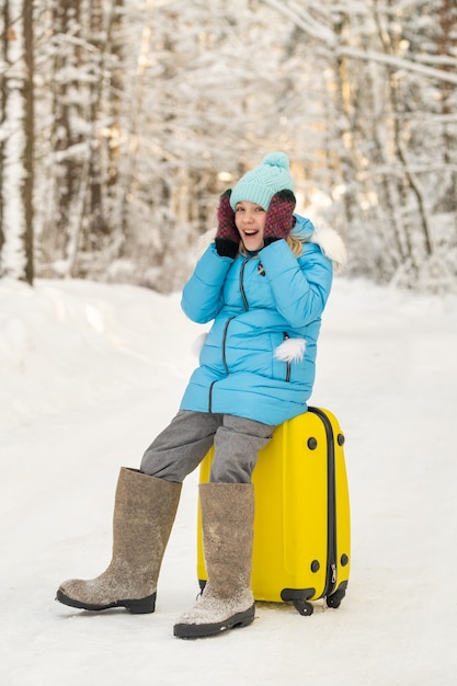 A girl in winter in felt boots sits on a suitcase on a frosty snowy day