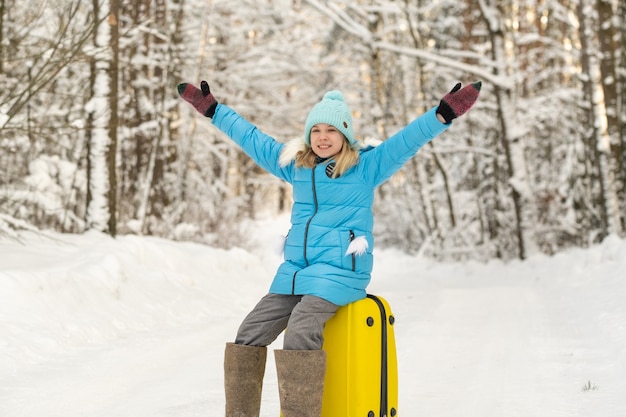 Девушка зимой в валенках сидит на чемодане в морозный снежный день.