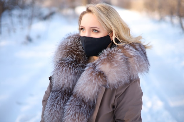 A girl in a winter fur coat with a black protective mask on her face