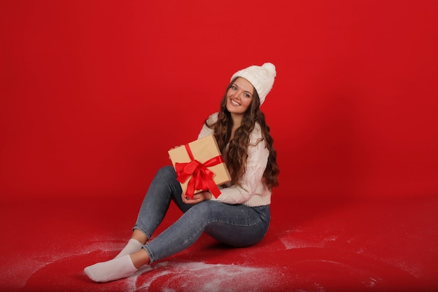 a girl in a winter hat and a knitted sweater holds a gift box of artificial snow in her hands