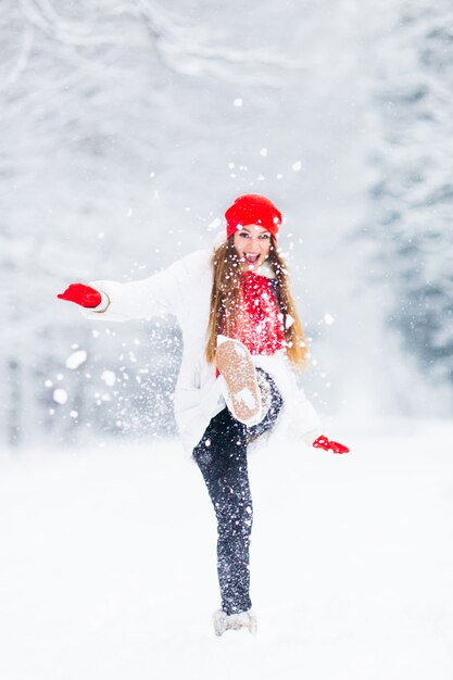 A girl in a winter jacket and warm accessories play with snow