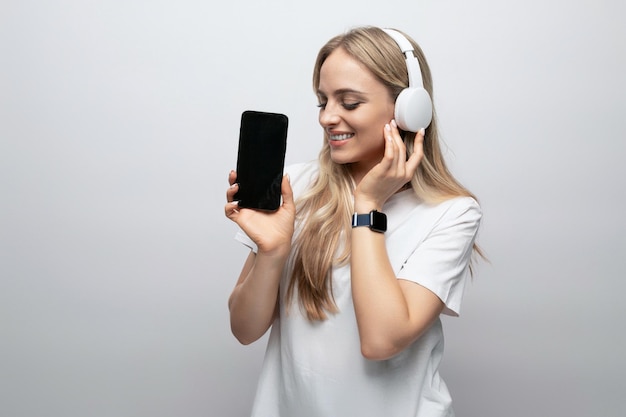 girl in wireless headphones with a smartphone in her hands with a black screen on a white background