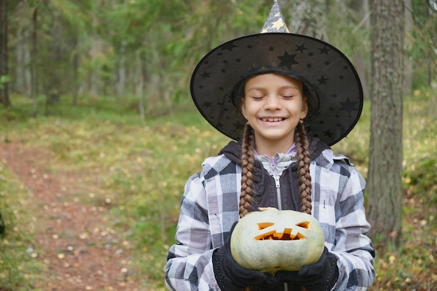 Girl in witch costume holding pumpkin lantern halloween concept girl in the forest playing with jack lantern