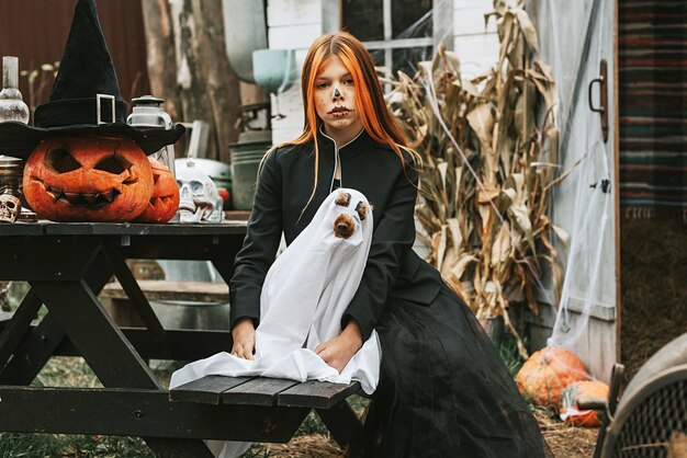 A girl in a witch costume with a dog in a ghost costume having fun on the porch of a house decorated to celebrate a Halloween party