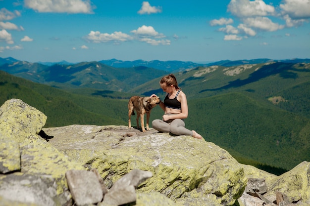 Фото Девушка с собакой на вершине горы, наблюдая красивый пейзаж с широко открытыми руками