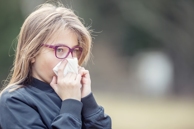 Ragazza con sintomi di allergia che soffia il naso. ragazza teenager che utilizza un tessuto in un parco.