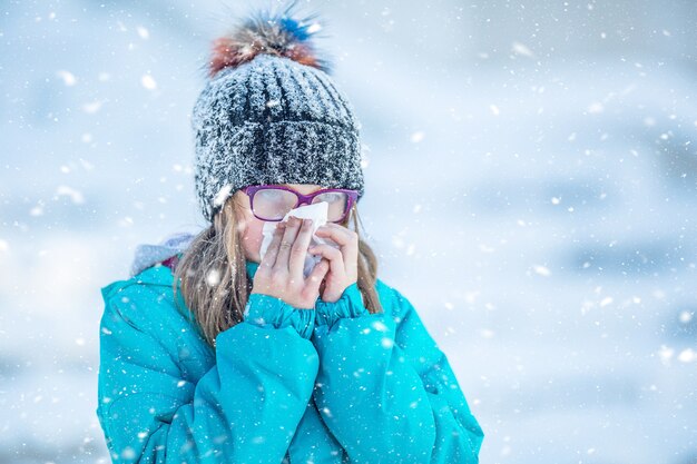 Photo girl with allergy symptom blowing nose. teen girl using a tissue in a winter park.