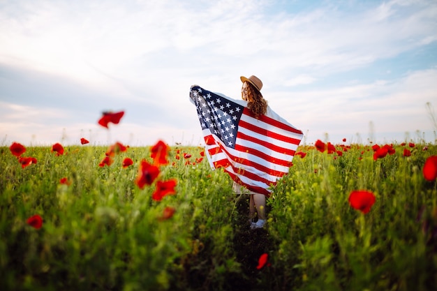 Girl with American flag posing in a poppy field 