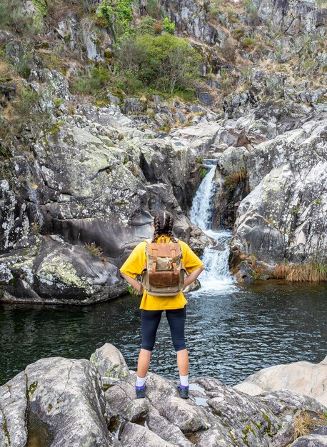 Girl with arms on hips looking at a waterfall