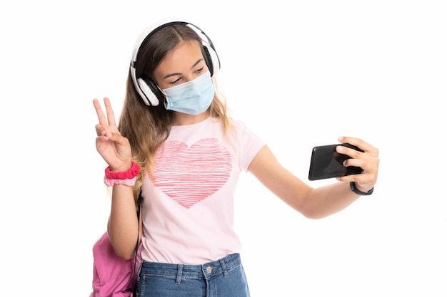 Ragazza con zaino, cuffie e maschera prendendo un selfie