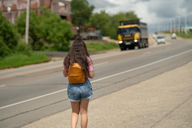 a girl with a backpack behind her shoulders walks along a road