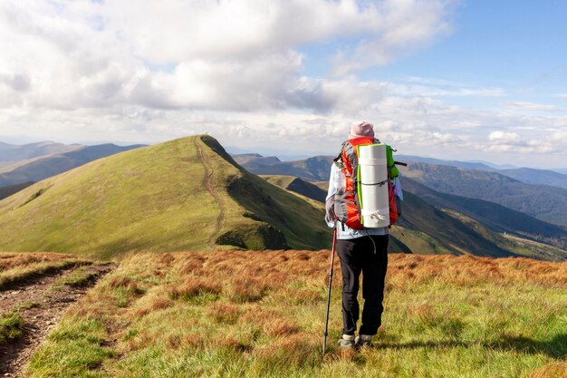 Девушка с рюкзаком и туристическим оборудованием стоит и смотрит на вершину горы