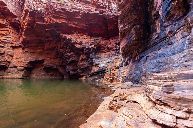 Girl with backpack hiking in a gorge on the edge of a rock pool\
in karijini national park, australia