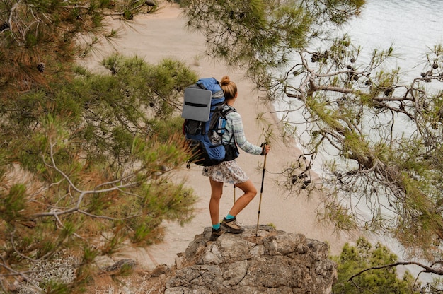 Girl with backpack and hiking sticks standing on on the rock among tree branches