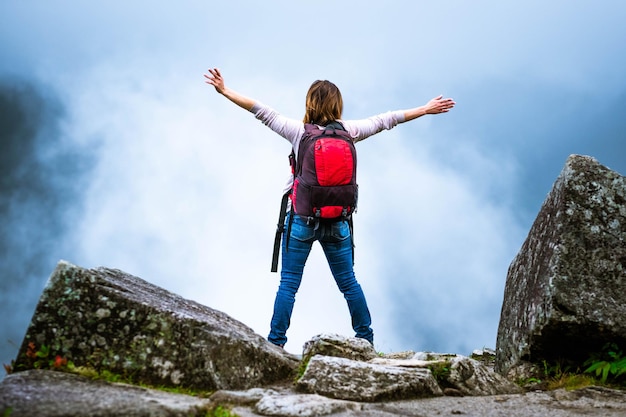 Girl with backpack in misty mountains with hands up