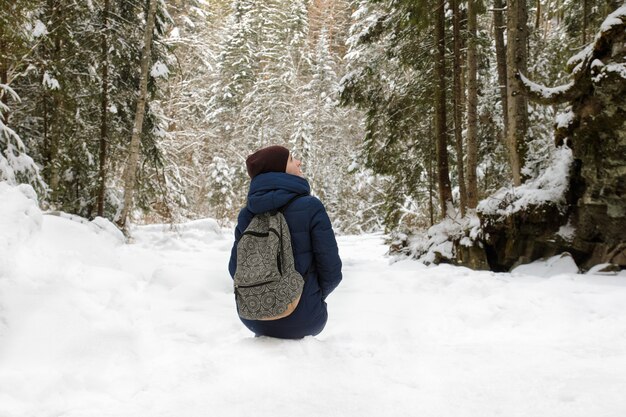 Girl with backpack sitting in a snow-covered coniferous forest. 