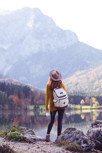 山の湖のほとりにバックパックを持った少女が立っている