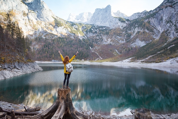 Photo girl with a backpack stands on the shore of a mountain lake