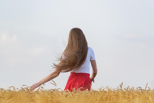 Girl with beautiful long hair walks through wheat field Health and strength of hair