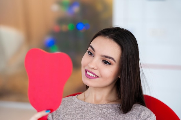 The girl with a beautiful smile looks in the mirror