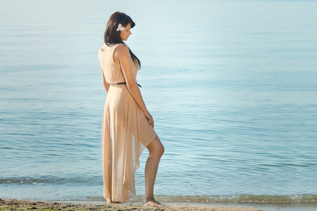 Девушка с черными волосами в бежевом платье на берегу синего моря