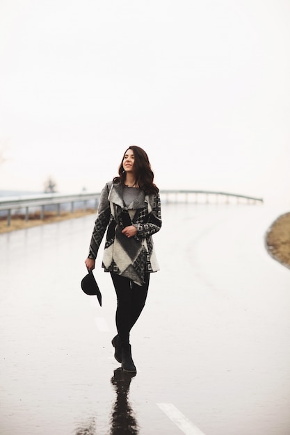 Girl with a black hat walking along the road on a rainy day