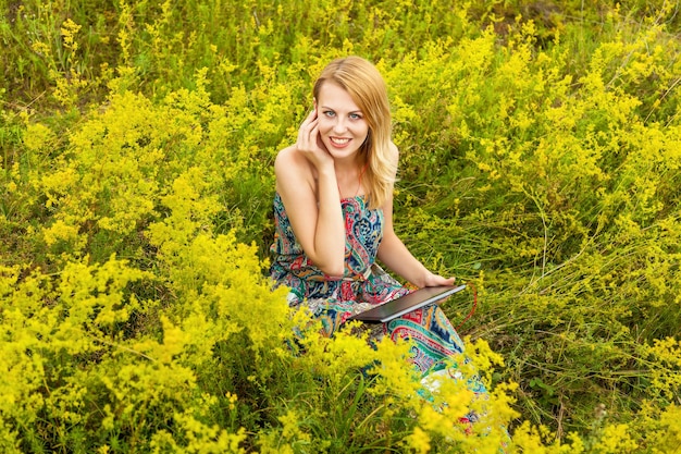 A girl with a black tablet in the field listening to music Girl in a field with a tablet