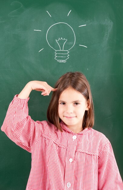 写真 黒板と彼女の頭の上に電球を持つ少女