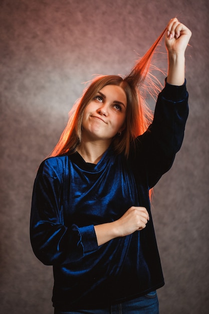 Girl with blond hair emotionally posing on a gray background. Her hair is lit in red