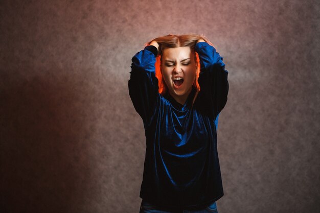 Girl with blond hair emotionally posing on a gray background. Her hair is lit in red