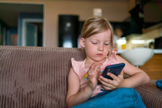 ブロンドの髪の少女は、自宅の子供とデジタルタブレットを持っている手の子供たちのスマートフォンで遊ぶ