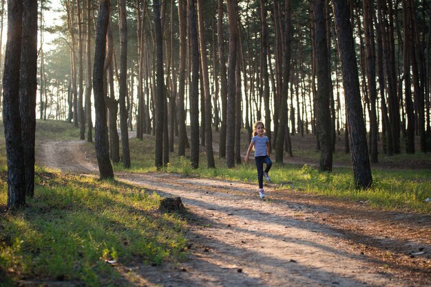 A girl with blond hair runs along a forest path jumping over all the branches in the morning