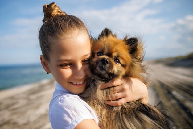 Girl with blond hair with smile hugs pomeranian dog with golden hair on seashore near Black Sea