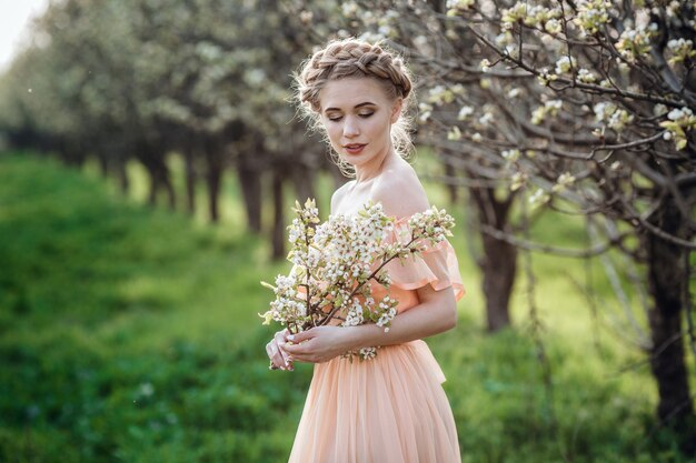 Girl with blonde hair in a light dress in flowering garden. concept of female spring fashion. 