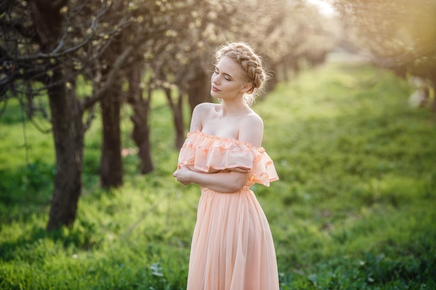 Girl with blonde hair in a light dress in flowering garden. concept of female spring fashion. 