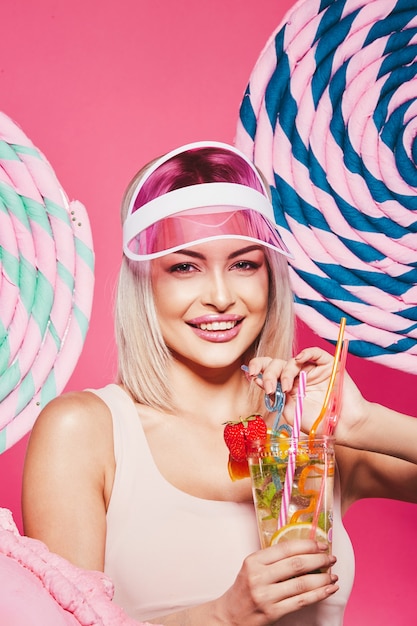 Girl with blonde hair wearing top and pink cap standing with huge sweet lollypops at pink