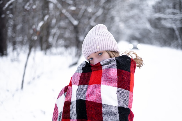 写真 雪に覆われた森の青い目をした少女が赤い格子縞のスカーフに包まれて不思議に見える