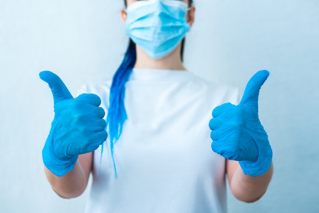 a girl with blue hair in gloves and a mask showing thumb up