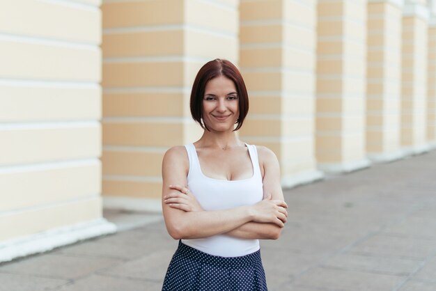 Girl with a bob hairstyle smiling with her arms crossed in a T-shirt walking in the city.