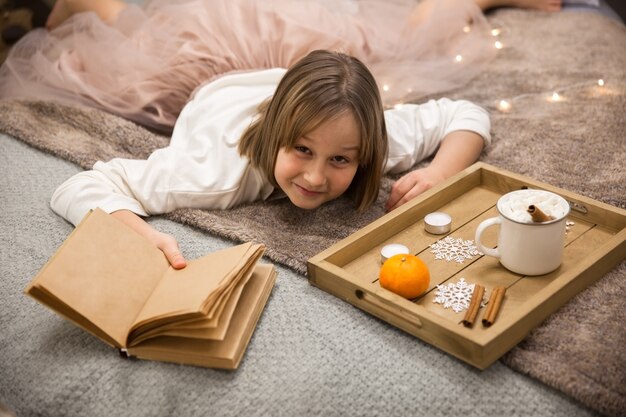 ベッドに横たわっている本を持つ少女、ベッドで朝食