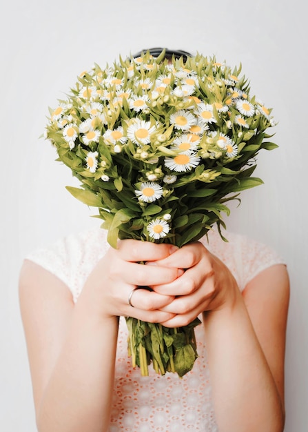 Girl with bouquet of camomile at white wall