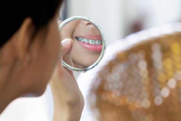 Girl with braces teeth looking to the mirror cleaning her teeths