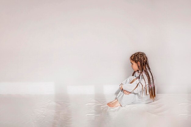 写真 白い壁に背を向けてベッドに座っているの毛を編んだ女の子