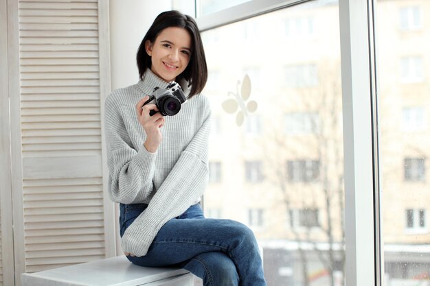 Girl with a camera sitting by the window