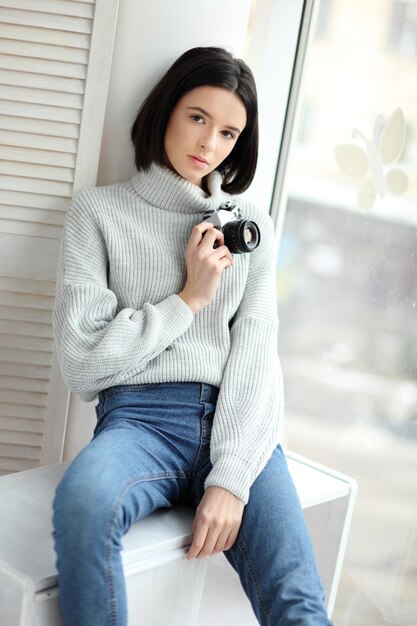 Girl with a camera sitting by the window