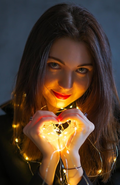 A girl with a Christmas garland. Light in hands, in the form of a heart