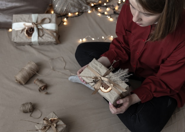 말린 꽃과 마른 오렌지로 장식된 크리스마스 선물을 받은 소녀는 공예 종이에 싸여 있습니다.