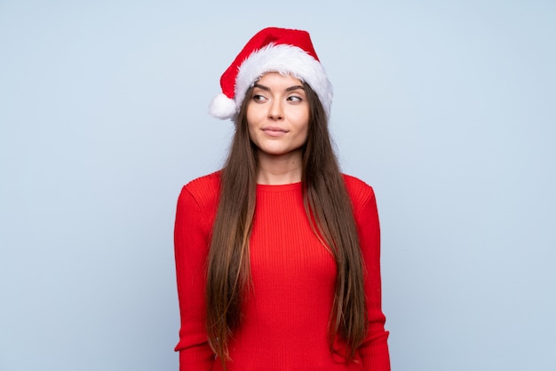 Girl with christmas hat over isolated blue standing and looking to the side